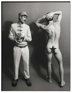A hotel bellhop in a uniform looking at a shirtless man standing with his back turned, featuring a star graphic on his hip.
