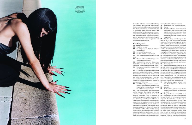 Woman with long dark hair and dramatic long black nails leans over a concrete edge next to bright turquoise water.