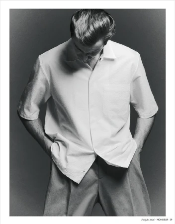 Model Ben Allen wearing a white short-sleeve shirt with hands in pockets against a grey studio backdrop for Monsieur Magazin Germany.