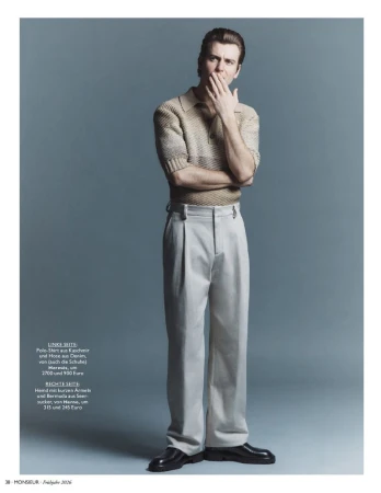 Full-length portrait of a male model wearing a knit polo shirt and light trousers against a grey seamless background