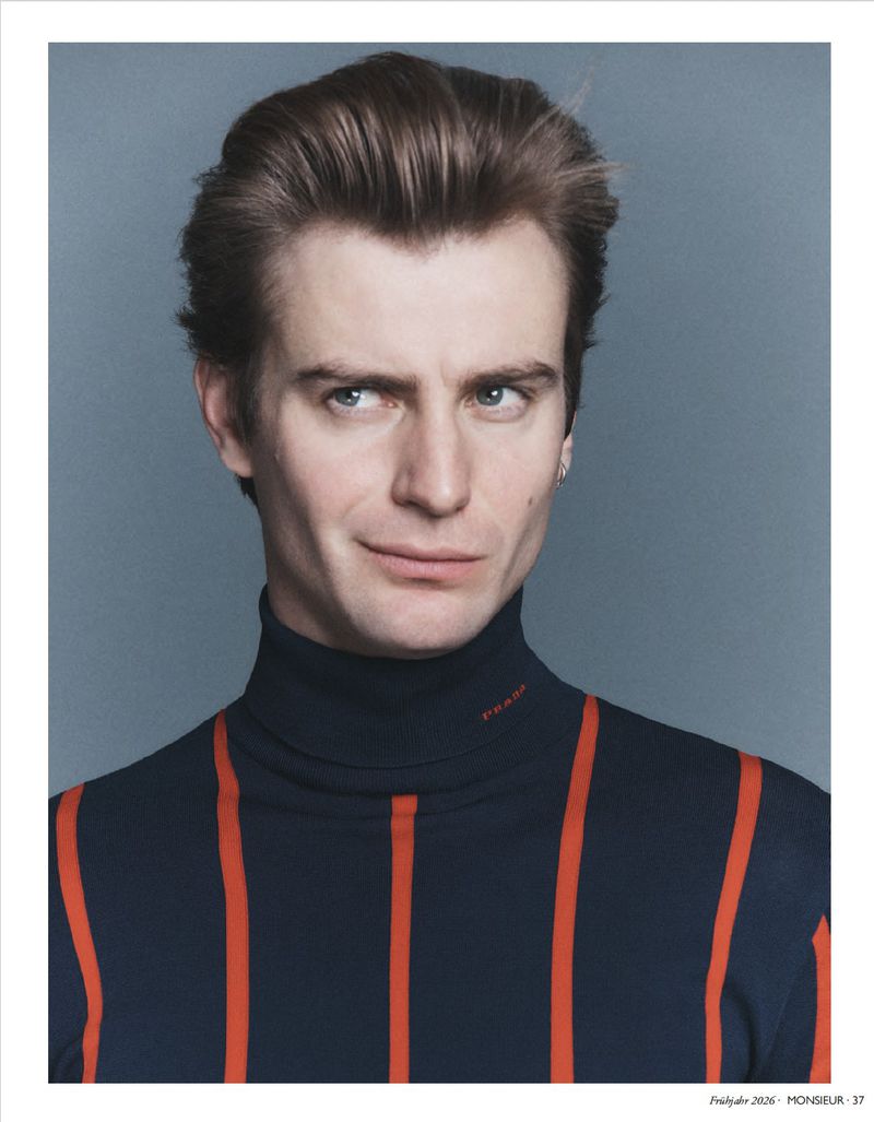 Portrait of a man wearing a dark turtleneck with red stripes against a grey backdrop