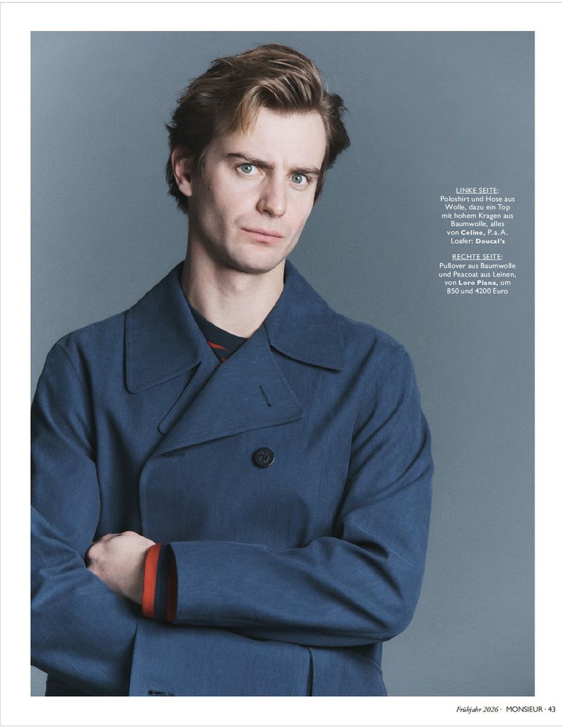 Portrait of a man wearing a blue coat with arms crossed against a plain grey backdrop