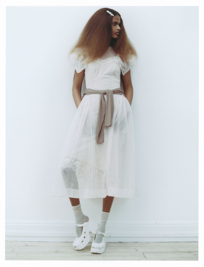 Model in white sheer midi dress with a sweater tied around the waist against a plain white background