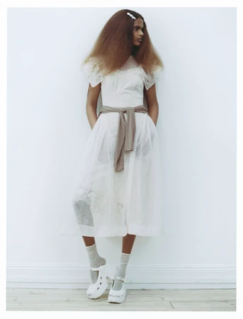 Model in white sheer midi dress with a sweater tied around the waist against a plain white background