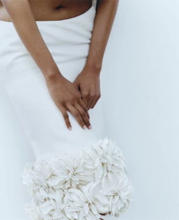 Close-up of a person wearing a white skirt with floral hem detail against a neutral studio backdrop