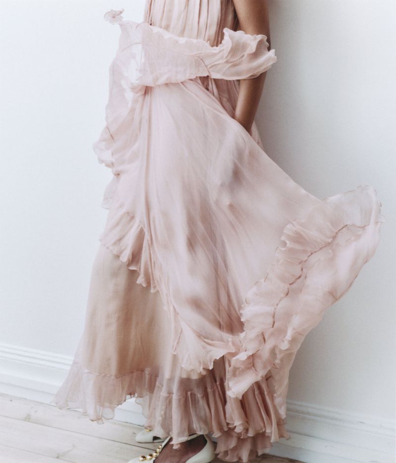 Model wearing a flowing pink ruffled gown against a plain white studio background.