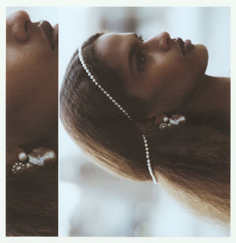 Close-up profile portrait of a model wearing a delicate pearl headband and pearl earrings against a soft neutral background.