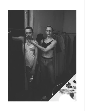 Black and white editorial portrait of two models posing backstage near a clothing rack for System Magazine