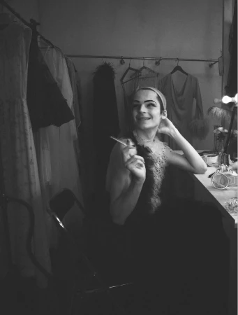 Model seated in a dressing room holding a cigarette, captured in black and white photography for System Magazine.