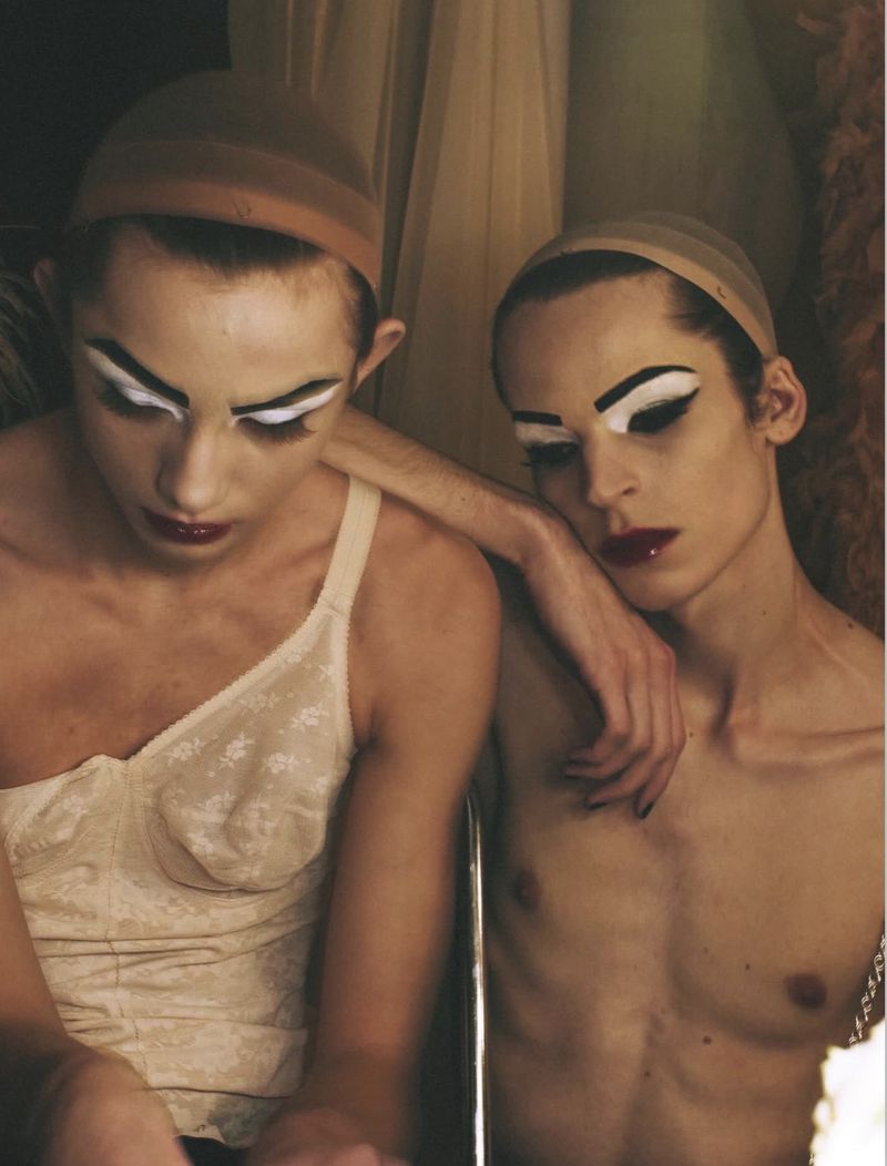 Two models wearing wig caps and dramatic theatrical makeup with white eye paint posing backstage for System Magazine.