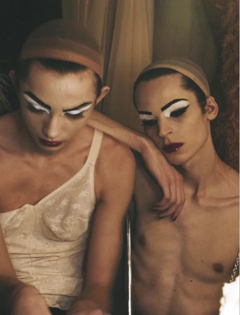 Two models wearing wig caps and dramatic theatrical makeup with white eye paint posing backstage for System Magazine.