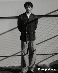 Man wearing a textured double-breasted blazer and trousers standing against a wall with chain-link shadows