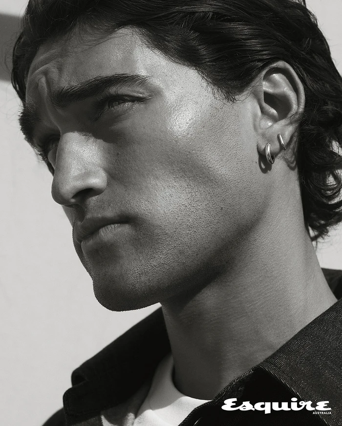 Close-up monochrome portrait of a man with dark wavy hair wearing hoop earrings and a dark collared shirt for Esquire Australia.