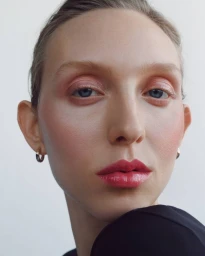 Close-up portrait of a woman wearing glossy pink lipstick and hoop earrings against a neutral background