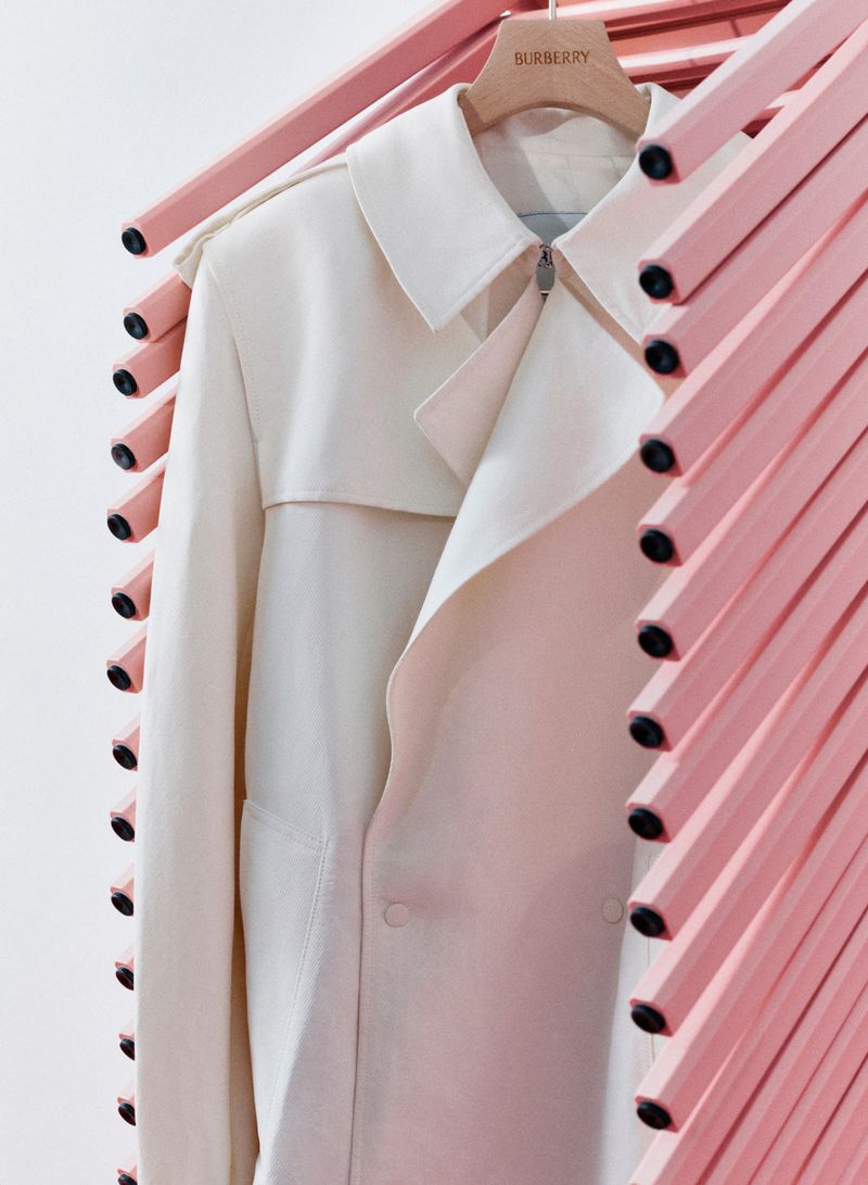 White trench coat hanging on wooden hanger framed by diagonal pink structural rods