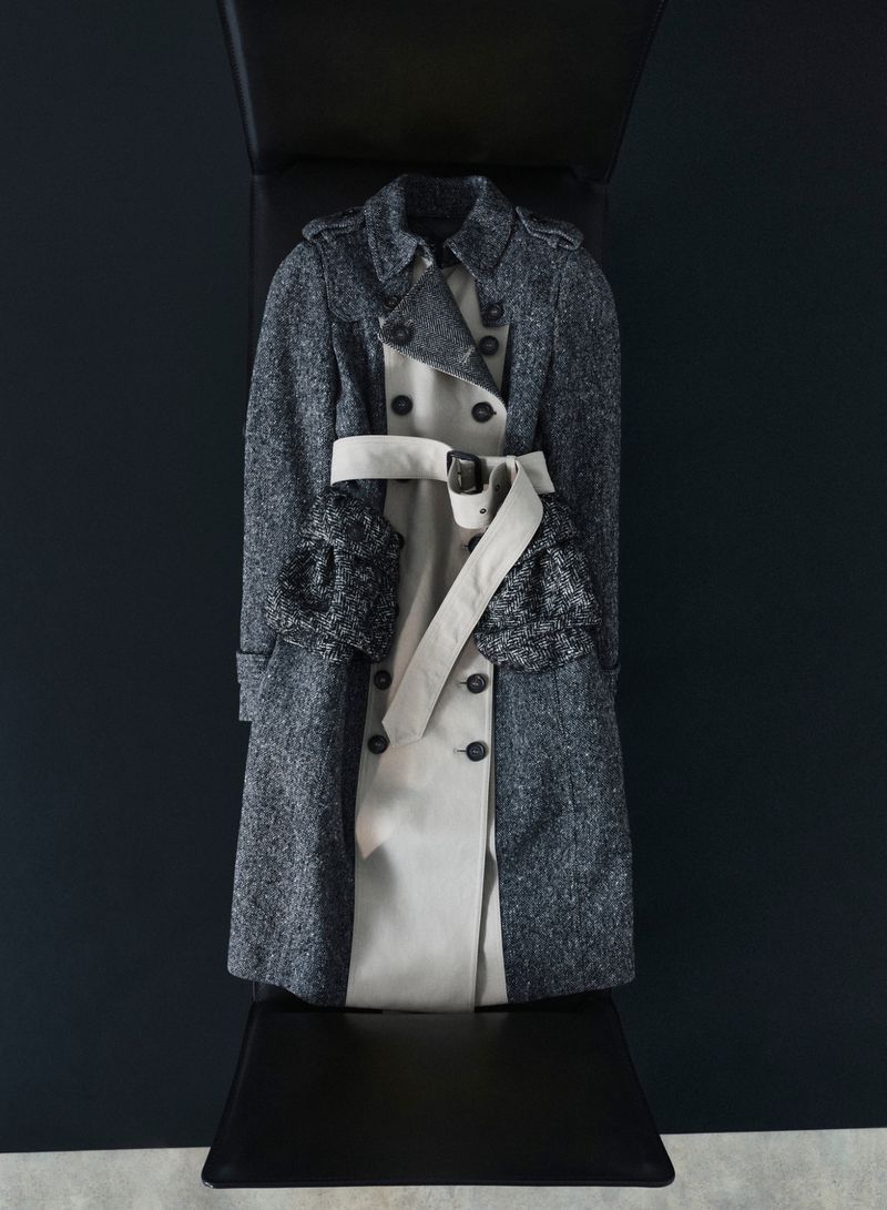 Layered trench coat with a dark tweed outer layer and light beige inner layer against a dark studio background