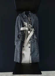 Layered trench coat with a dark tweed outer layer and light beige inner layer against a dark studio background