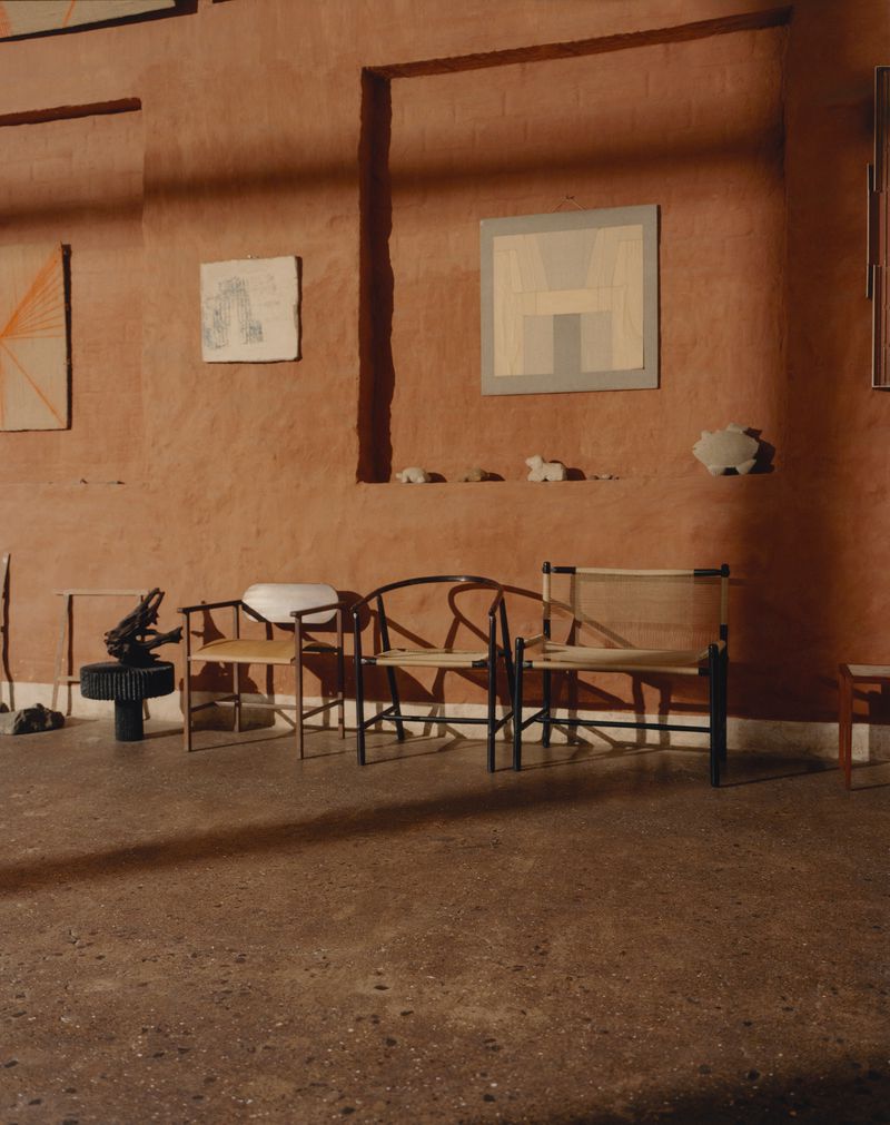 Interior shot showcasing minimalist chairs arranged against a textured terracotta-colored wall with framed artworks.
