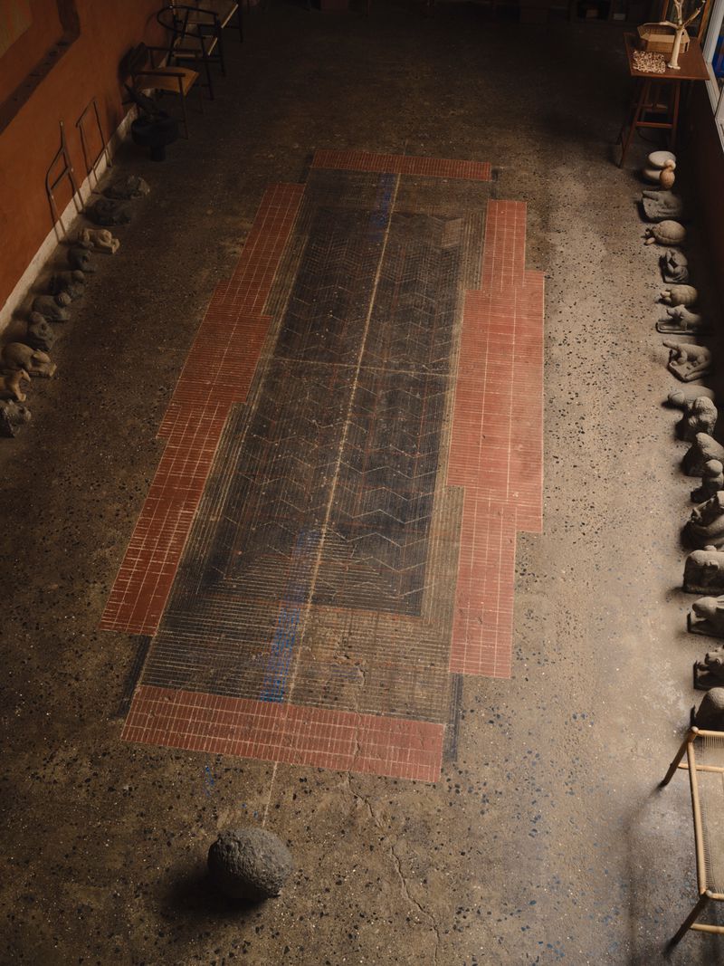 High-angle interior view of an architectural space featuring a decorative tiled floor and rows of sculptures along the walls.