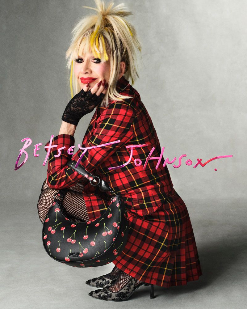 Woman in red plaid coat crouching with black cherry handbag and lace gloves and shoes against grey background, Betsey Johnson text
