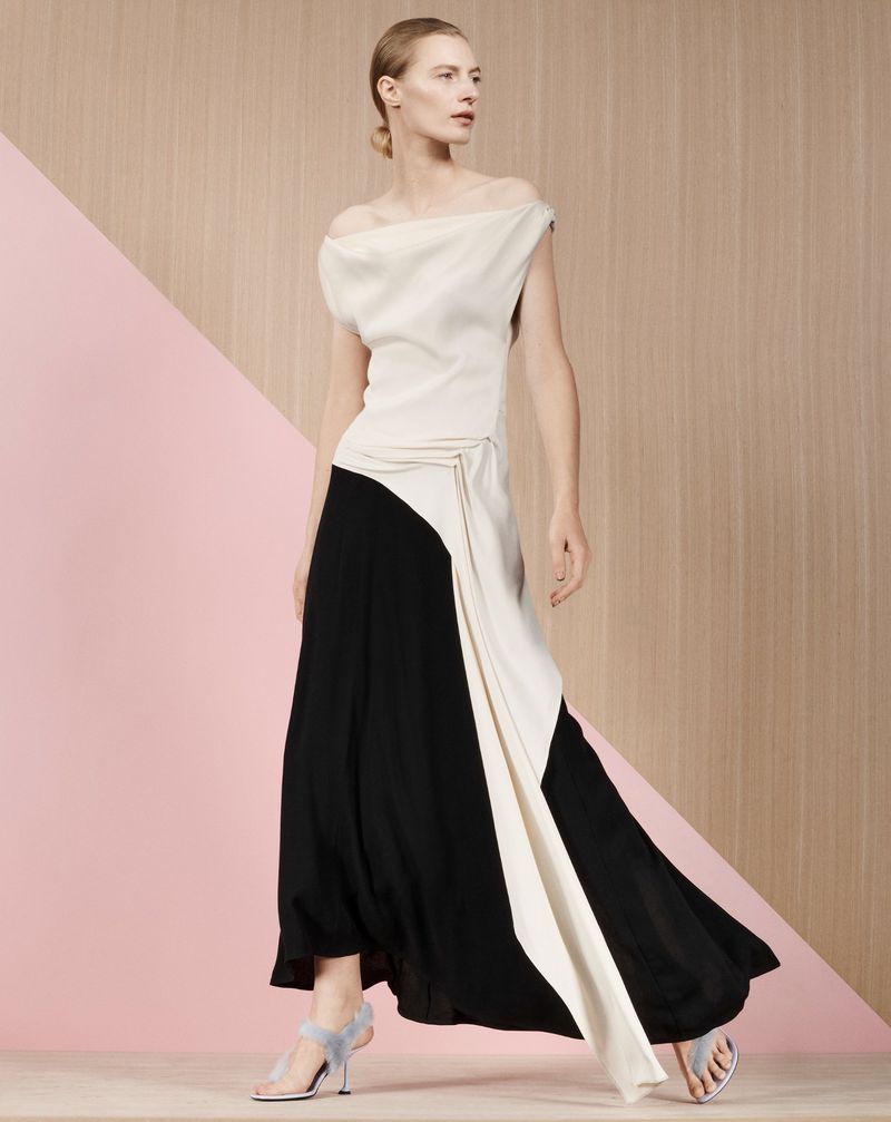 Model Julia Nobis wearing an off-the-shoulder black and white dress against a geometric pink and wood-textured backdrop.