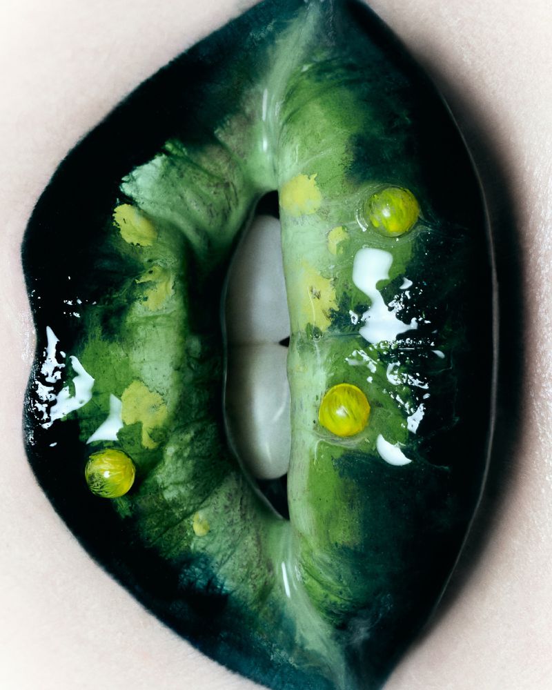 Close-up macro shot of dark green painted lips adorned with small yellow beads and glossy highlights for Tush Magazine.