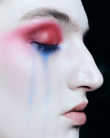 Close-up profile of a model with dramatic red eyeshadow and blue streaks running down her face for Tush Magazine.