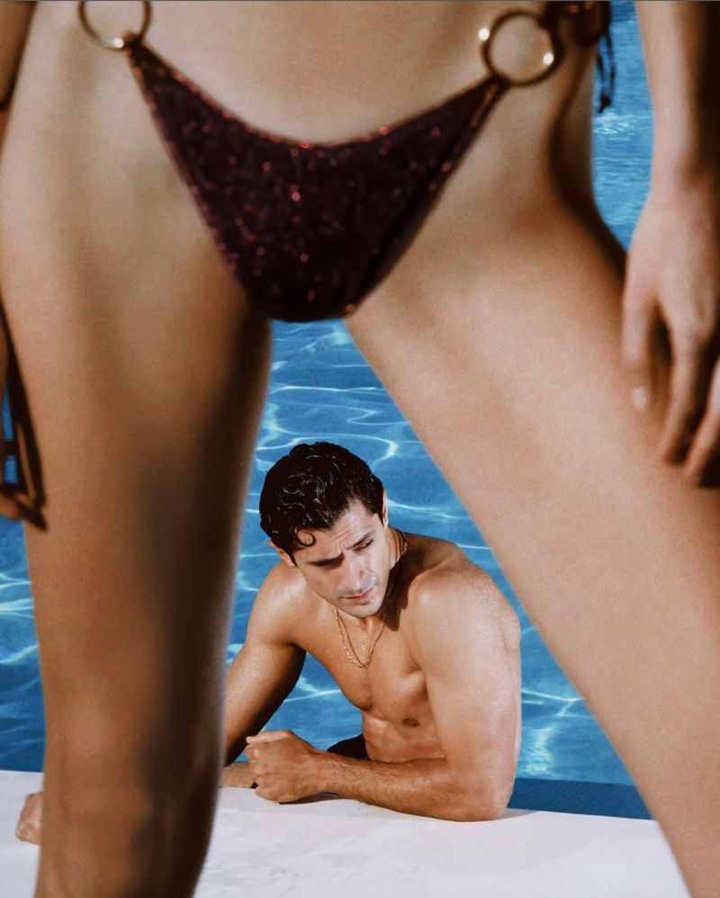 Close-up of a model in a dark bikini bottom with a man posing in a swimming pool behind for 70s Mania