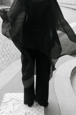 Model in flowing black sheer cape and wide trousers standing on a paved street