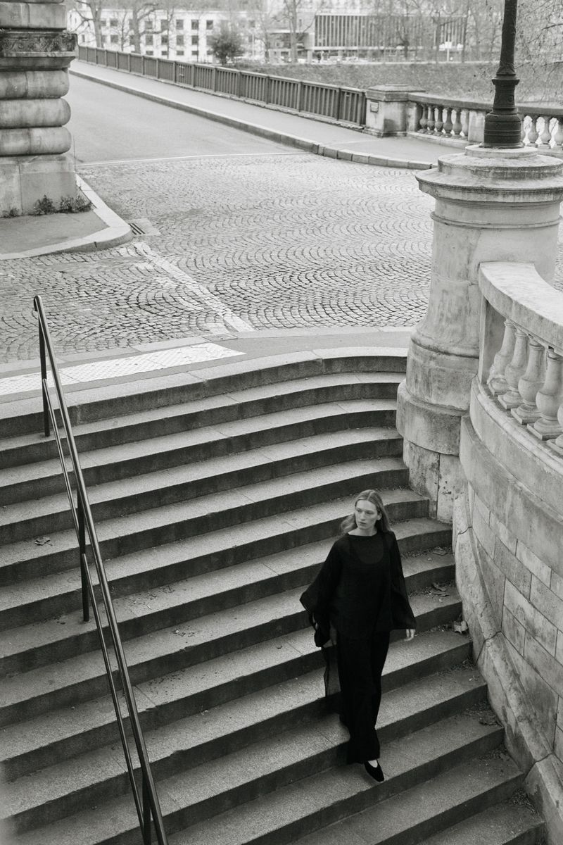 Model Liz Kennedy walking down classical stone outdoor stairs wearing a black outfit for Almada S/S 2026