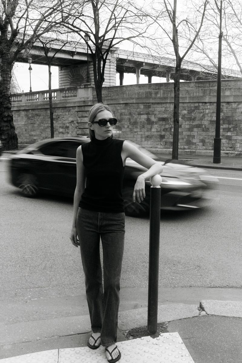 Model Liz Kennedy posing on a city street next to a bollard with a blurred car passing in the background, captured in monochrome.