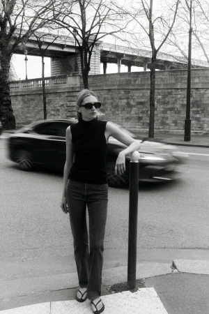 Model Liz Kennedy posing on a city street next to a bollard with a blurred car passing in the background, captured in monochrome.