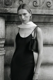 Model wearing black slip dress and light scarf holding handbag against stone architectural background
