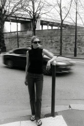 Model Liz Kennedy posing on a city street next to a bollard with a blurred car passing in the background, captured in monochrome.