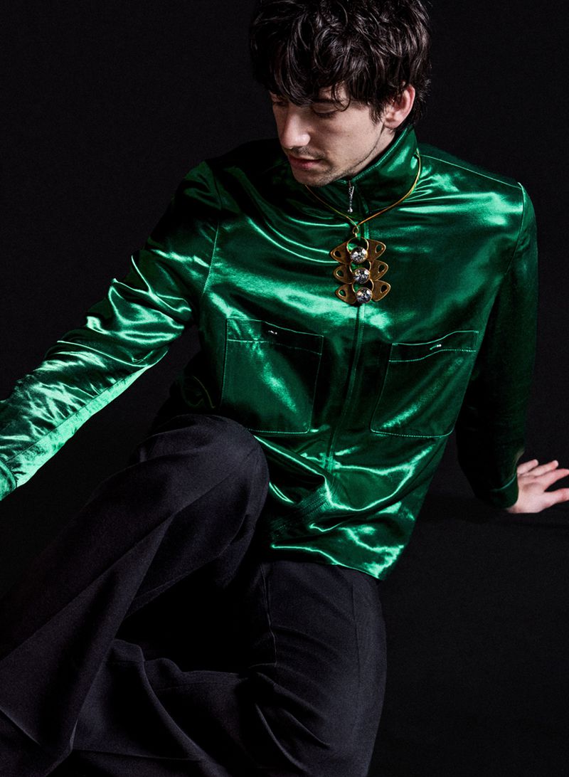Milo Manheim wearing a glossy emerald green satin jacket and dark trousers against a plain black background for V Man.