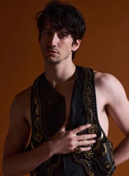Portrait of a man wearing a black leather vest with ornate gold embroidery against a solid brown background