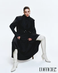 Model wearing a dark pinstripe coat and white thigh-high boots seated against a plain white background for L'Officiel Argentina.