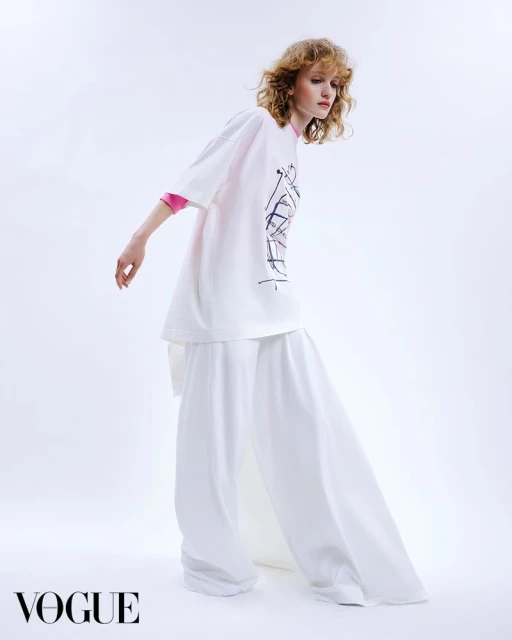 Fashion editorial shot: A woman in a white oversize t-shirt and palazzo pants poses against a stark white backdrop in a studio setting.