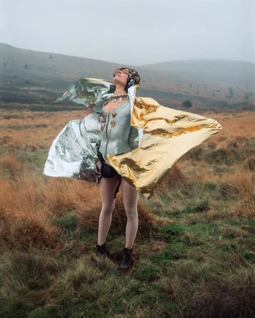 Model standing on a misty moor wearing a reflective cape and structured garment captured by Siân Davey.
