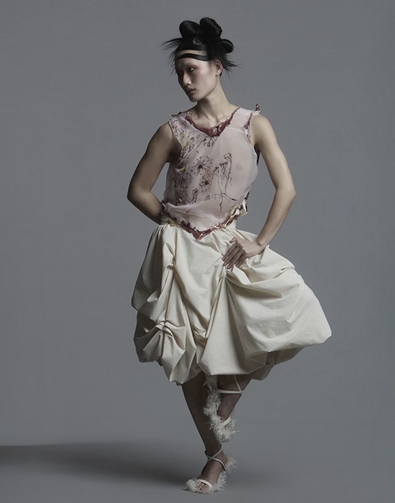 Model in sheer pink top and voluminous cream skirt posing against grey background for Vingt Sept Magazine editorial