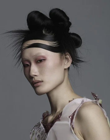 Portrait of an Asian woman with elaborate dark sculpted hair and pink eyeshadow against a grey studio backdrop