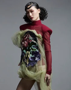 Asian woman wearing a red mock-neck top and sheer green draped dress against a grey backdrop for Vingt Sept Magazine