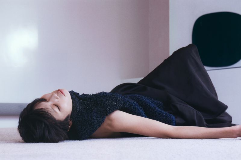 Model Kayako Higuchi lying on a light surface wearing a dark textured top and skirt for CR Fashion Book.