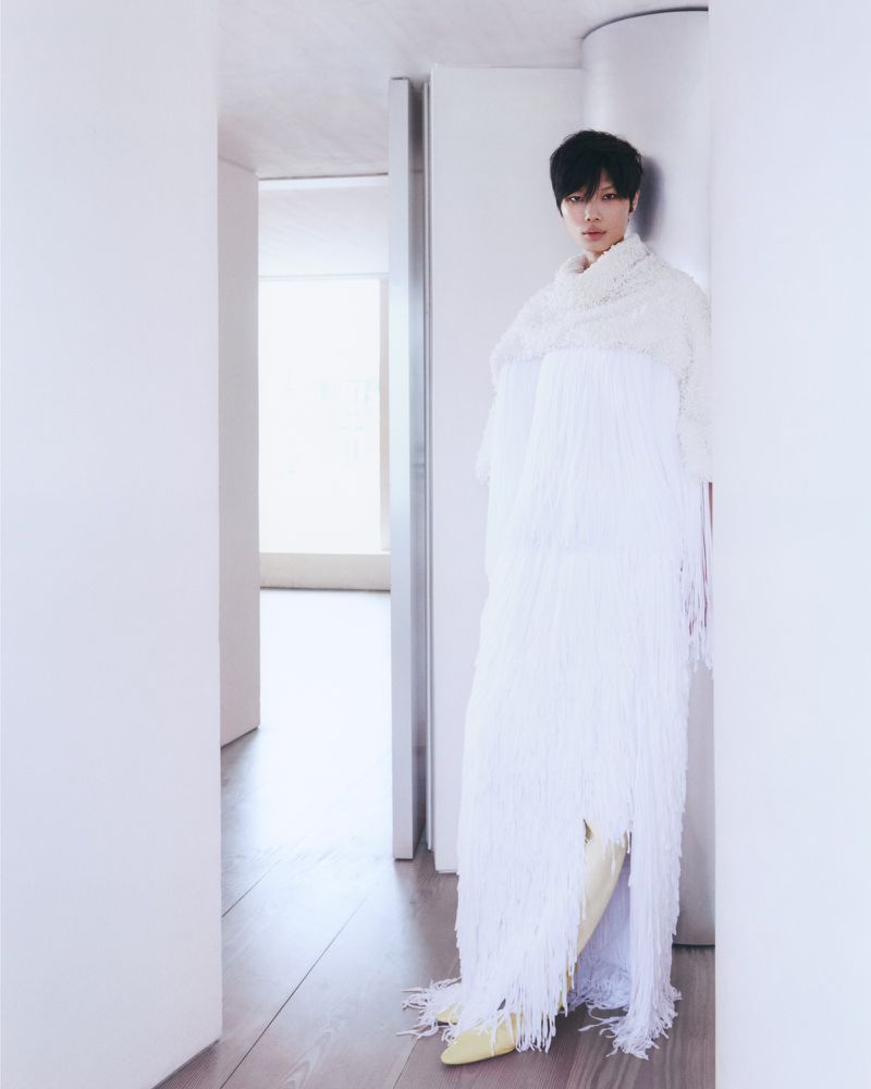 Model with short dark hair wearing a long white fringe dress standing in a white minimalist architectural interior