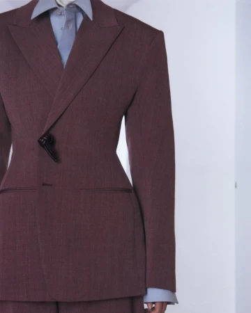 Close-up of a tailored maroon blazer and light blue collared shirt on a model against a neutral studio background.