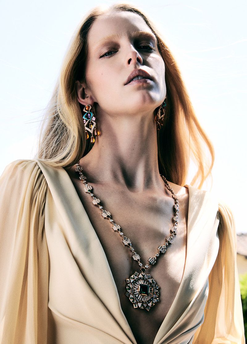 Close-up of a blond adult woman wearing antique gold jewelry, posed outdoors under natural light, in a fashion editorial style.