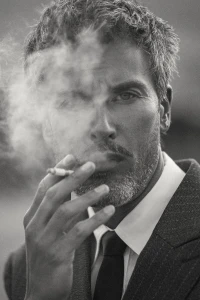 Portrait of a man in a pinstripe suit smoking a cigarette with smoke swirling past his face