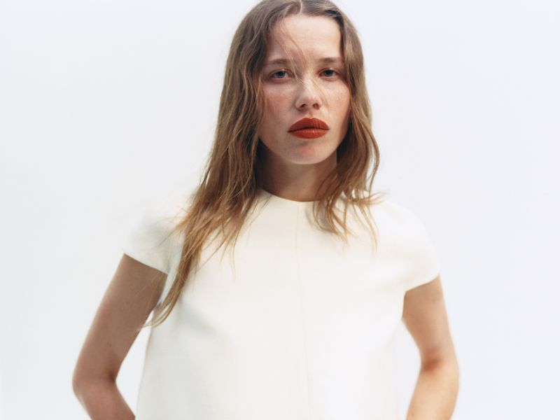 Close-up portrait of a woman with red lipstick wearing a white top against a white studio seamless background