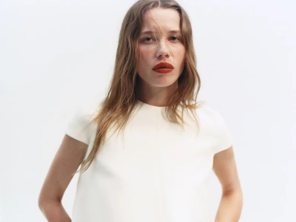 Close-up portrait of a woman with red lipstick wearing a white top against a white studio seamless background
