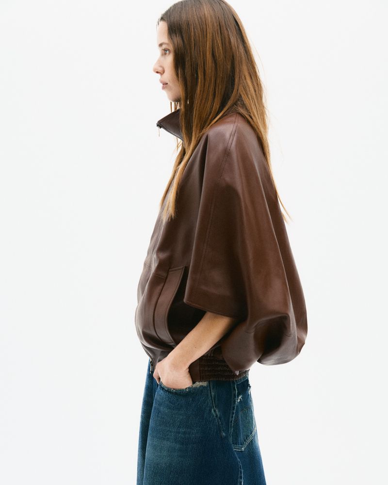Model in brown leather jacket and blue denim jeans standing against white seamless background
